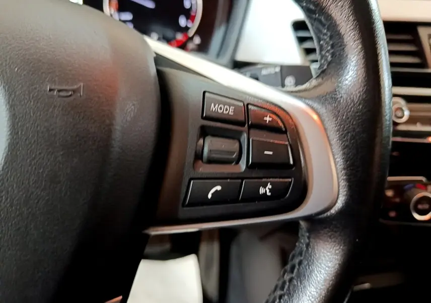 Gros plan sur les commandes du volant en cuir noir d'une BMW X1 sDrive16d Business Design 2020.