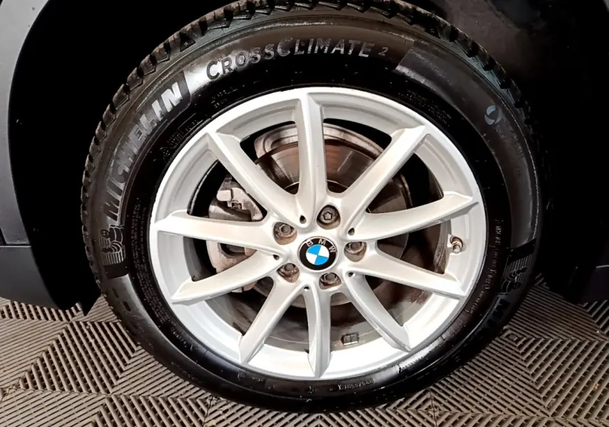 Gros plan sur la roue avant gauche noire d’un BMW X1 2020 avec jante alliage argentée et logo BMW central.