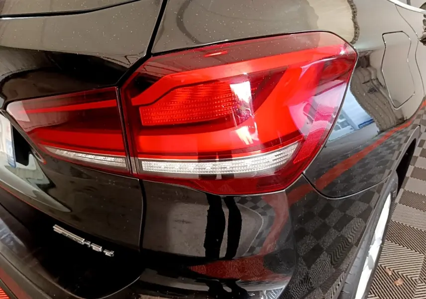 Gros plan sur le feu arrière droit d’un BMW X1 noir, mettant en valeur la finition brillante et les lignes du coffre arrière.