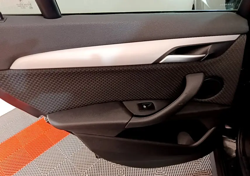 Gros plan sur la porte intérieure côté gauche d'un BMW X1 noir, avec poignée et bouton de verrouillage visibles.