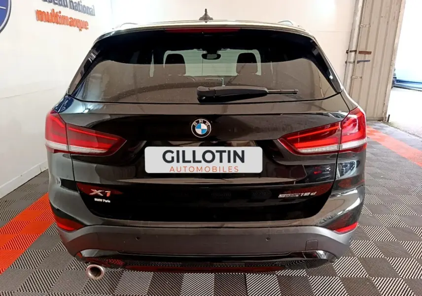 Vue arrière d'un BMW X1 noir sDrive16d avec feux LED et sortie d'échappement visible en intérieur showroom.
