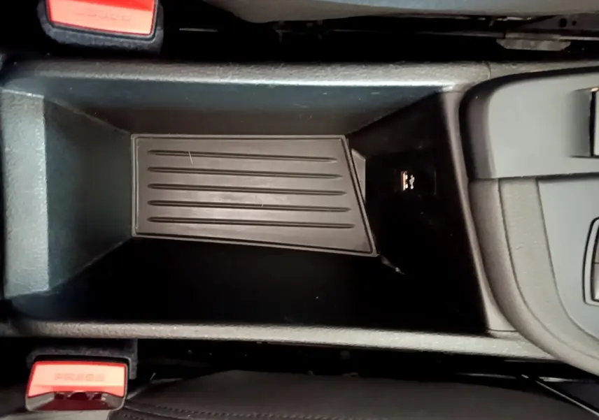 Gros plan sur le rangement central noir du BMW X1 sDrive16d Business Design avec prises USB et boutons de ceinture rouge.