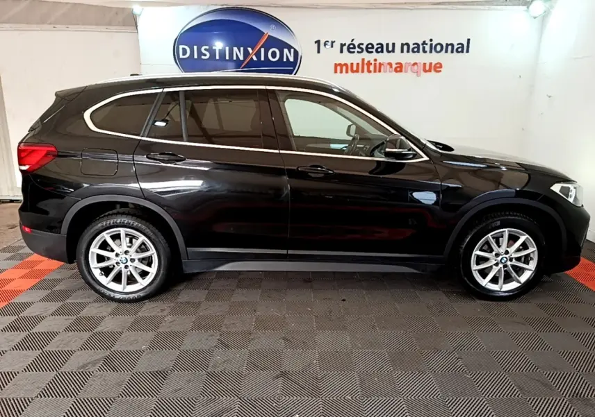 Profil droit d'un BMW X1 noir 2020 garé en intérieur, soulignant ses lignes élégantes et ses jantes argentées.