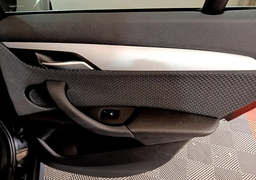 Détail de la porte intérieure côté gauche du BMW X1 noir, avec poignée argentée et bouton de verrouillage.