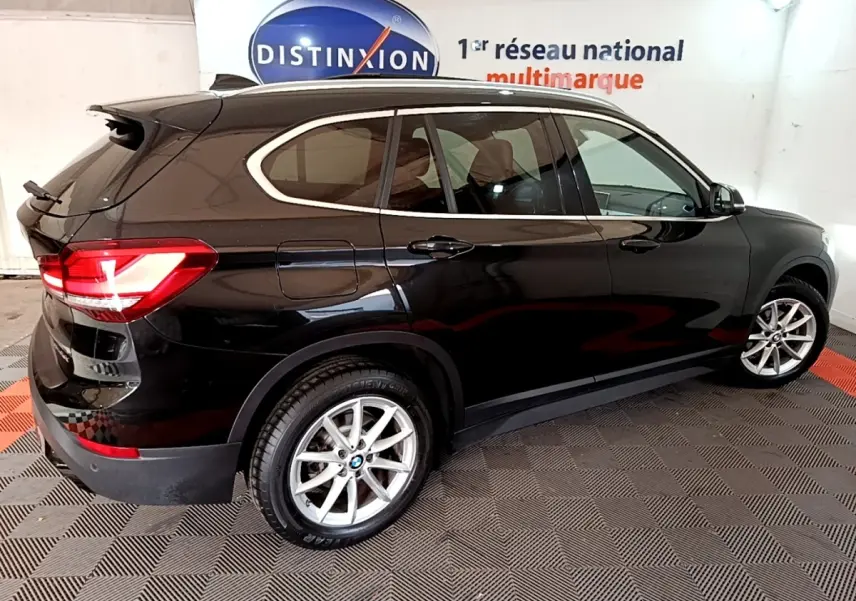 BMW X1 sDrive16d noir vue de profil côté gauche en intérieur avec jantes alliage et feux arrière LED allumés