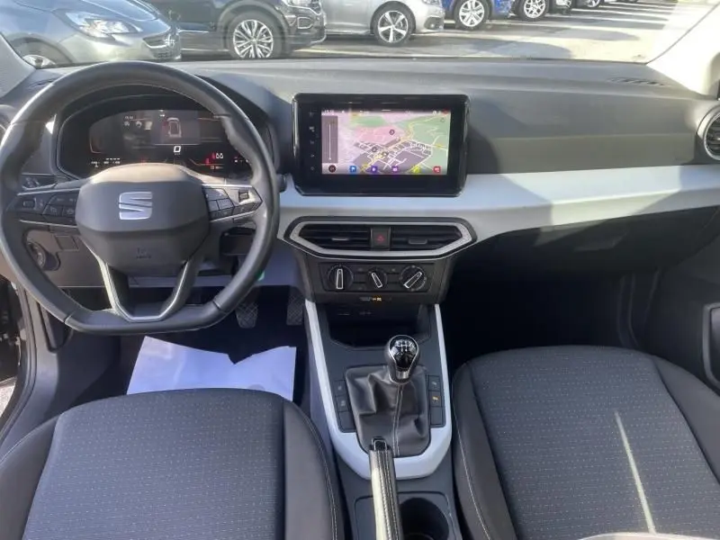 Vue intérieure avant du SEAT Arona noir 2023, tableau de bord avec écran tactile et levier de vitesse manuel.