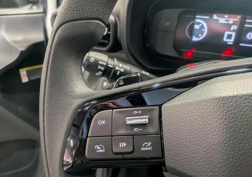 Gros plan sur les commandes au volant noir du Toyota Proace City blanc, avec tableau de bord numérique en arrière-plan.