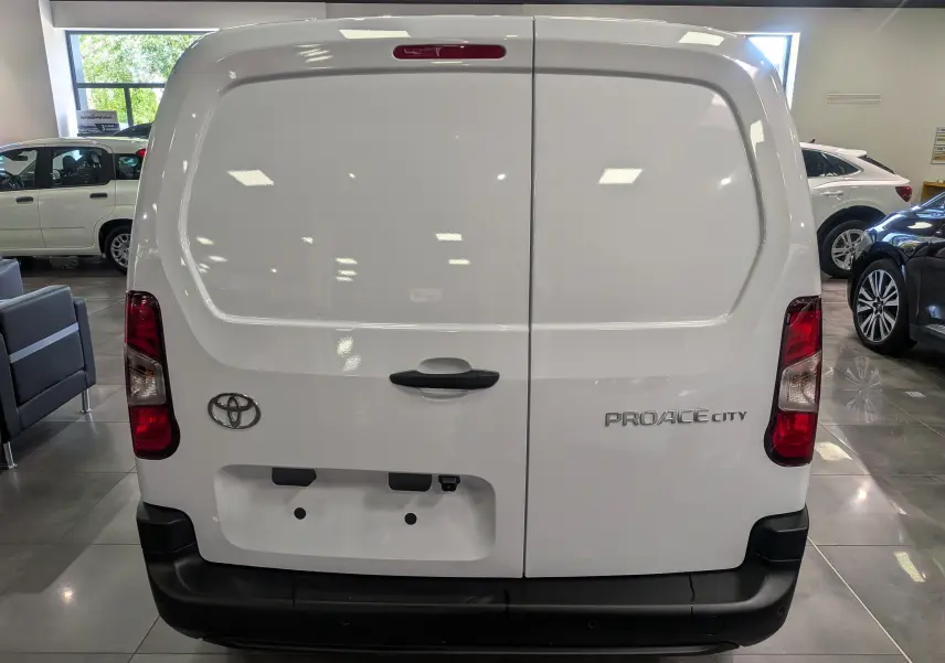 Vue arrière du Toyota Proace City blanc glacier, avec portes battantes et logo distinctif visible en concession.