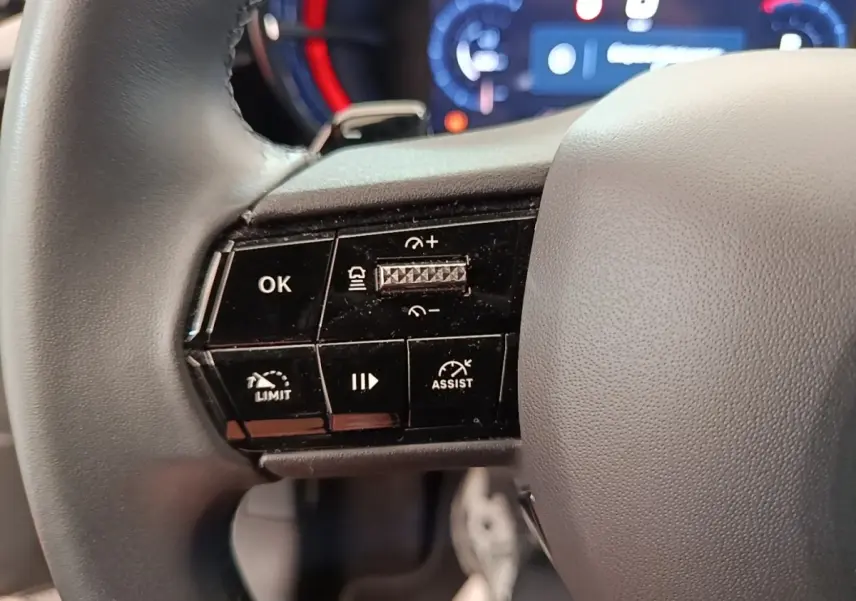 Gros plan sur le côté gauche du volant cuir noir de l'Alfa Romeo Junior 2024, avec commandes multifonctions et tableau de bord flou.
