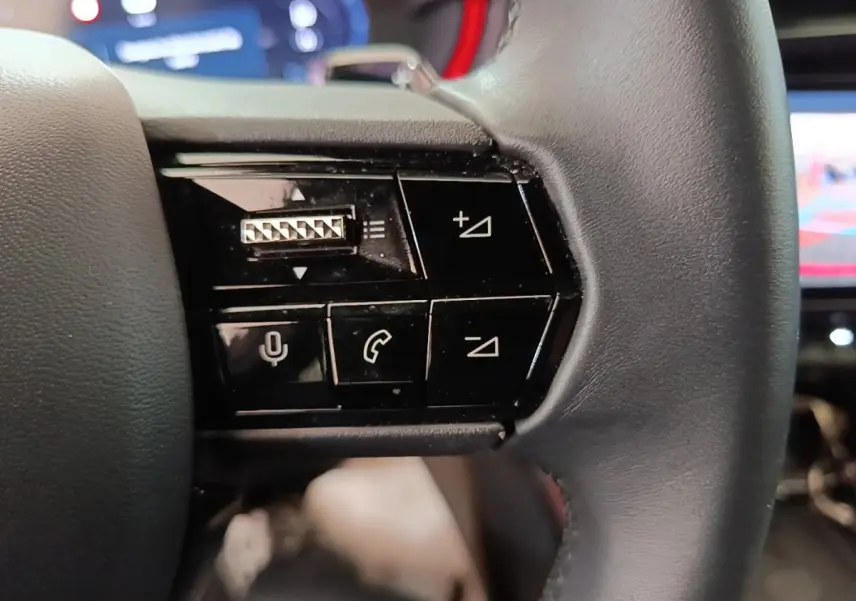 Gros plan sur les commandes noires du volant cuir de l'Alfa Romeo Junior 1.2 Ibrida 2024, avec boutons multifonctions.