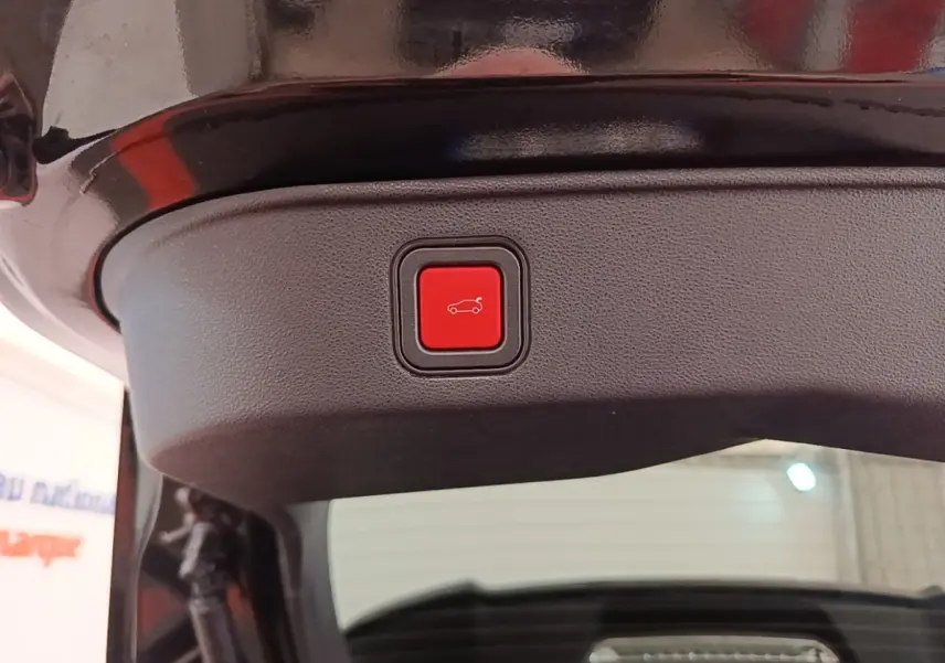 Gros plan sur le bouton rouge d'ouverture électrique du coffre, sur la partie intérieure du hayon noir d'une Alfa Romeo Junior 2024.