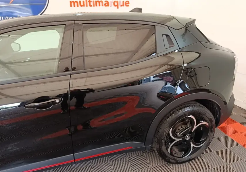 Vue latérale droite de l'Alfa Romeo Junior 1.2 Ibrida noire, avec jantes distinctives et ligne rouge décorative sur le bas de caisse.