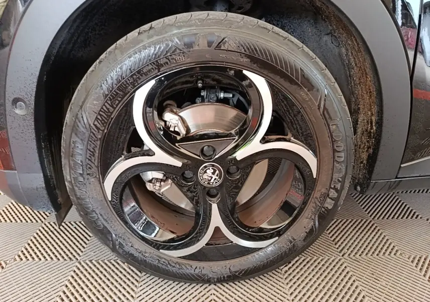 Gros plan sur la roue avant droite noire d'une Alfa Romeo Junior 1.2 Ibrida 136ch Speciale DCT6 avec jante bi-ton distinctive.