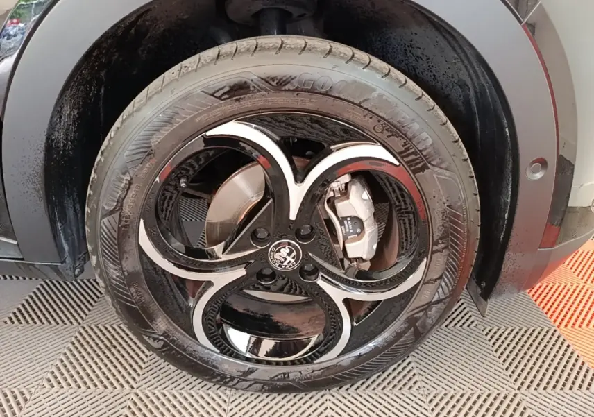 Gros plan sur la roue avant droite noire d'une Alfa Romeo Junior 1.2 Ibrida avec jante au design distinctif en forme de trèfle.