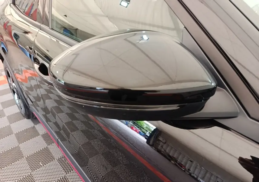 Rétroviseur côté gauche noir brillant d'une Alfa Romeo Junior 2024, avec reflet de l'environnement intérieur.