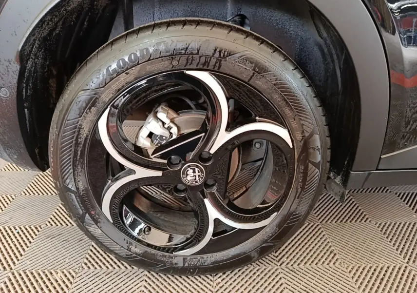 Gros plan sur la roue avant gauche noire de l'Alfa Romeo Junior 1.2 Ibrida 136ch Speciale DCT6 2024.