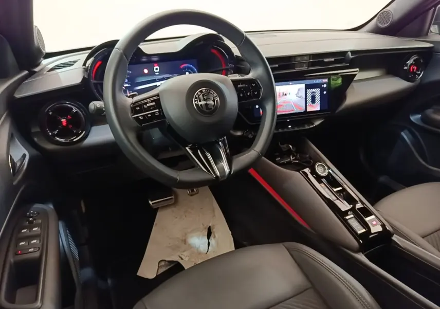 Vue intérieure avant gauche de l'Alfa Romeo Junior 1.2 Ibrida 2024, volant cuir, écran tactile et tableau de bord numérique.