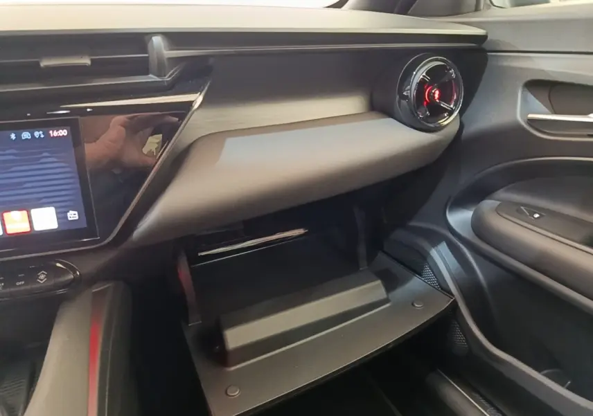 Intérieur côté passager de l'Alfa Romeo Junior 2024 noir, avec boîte à gants ouverte et aérateur rond rouge.