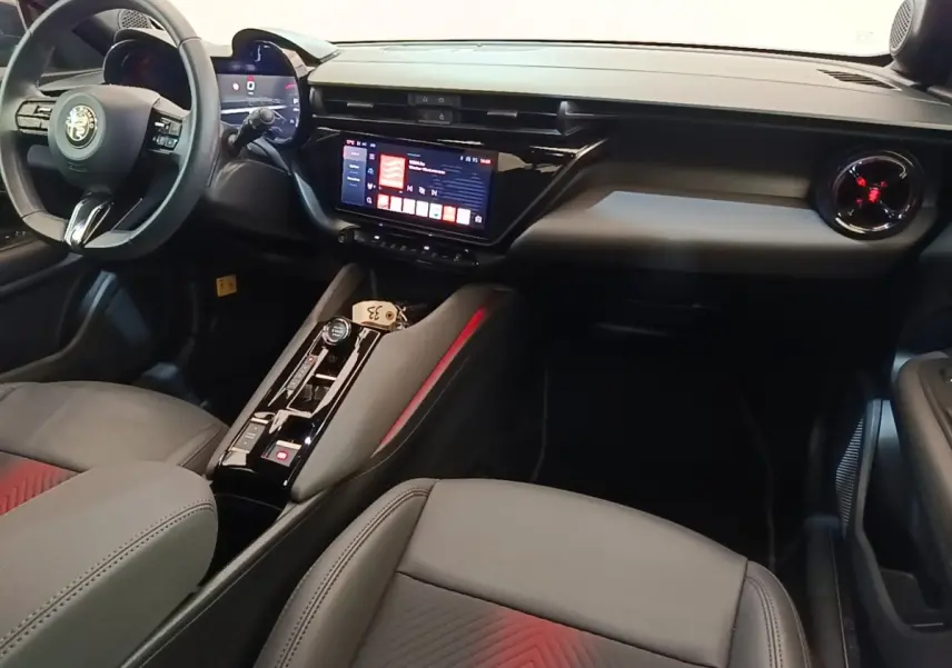 Vue intérieure côté conducteur de l'Alfa Romeo Junior 2024, tableau de bord noir avec écran tactile et volant cuir multifonctions.