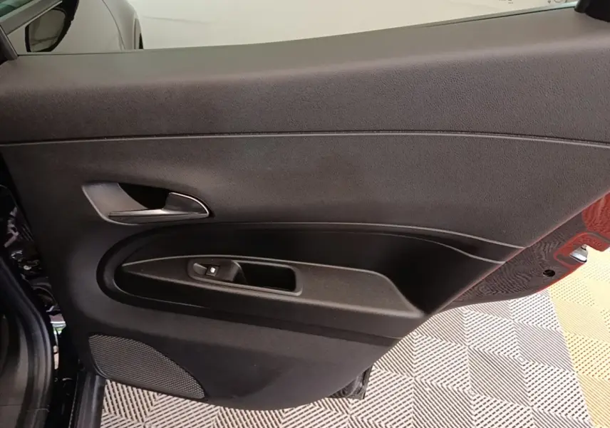 Vue intérieure sur la porte côté gauche noire de l'Alfa Romeo Junior 2024 avec poignée et commande de vitre électrique.
