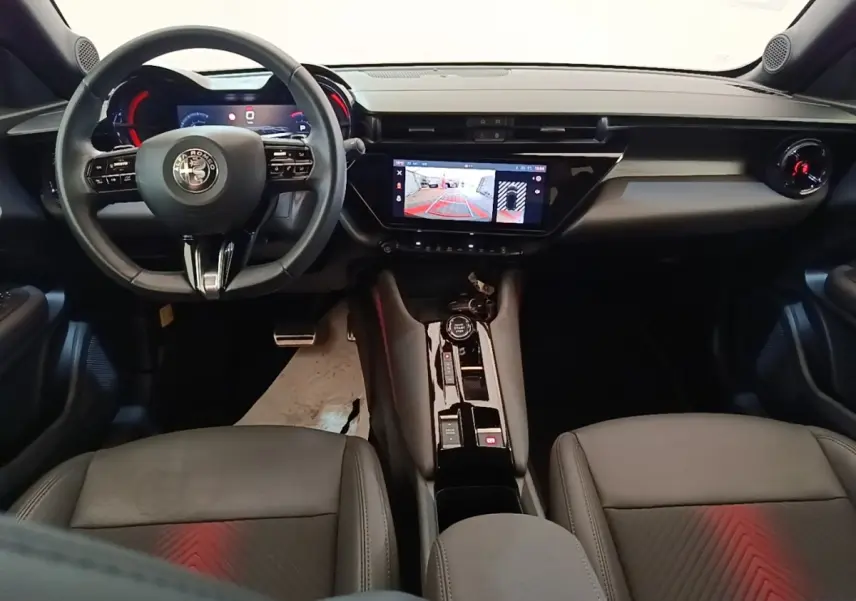 Vue intérieure avant de l'Alfa Romeo Junior 2024, tableau de bord noir avec écran tactile et volant cuir multifonctions.