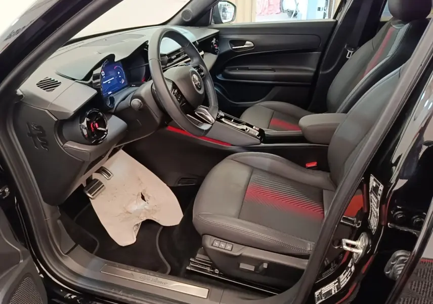 Vue intérieure côté conducteur de l'Alfa Romeo Junior 1.2 Ibrida noire, avec sièges en cuir et tableau de bord digital.