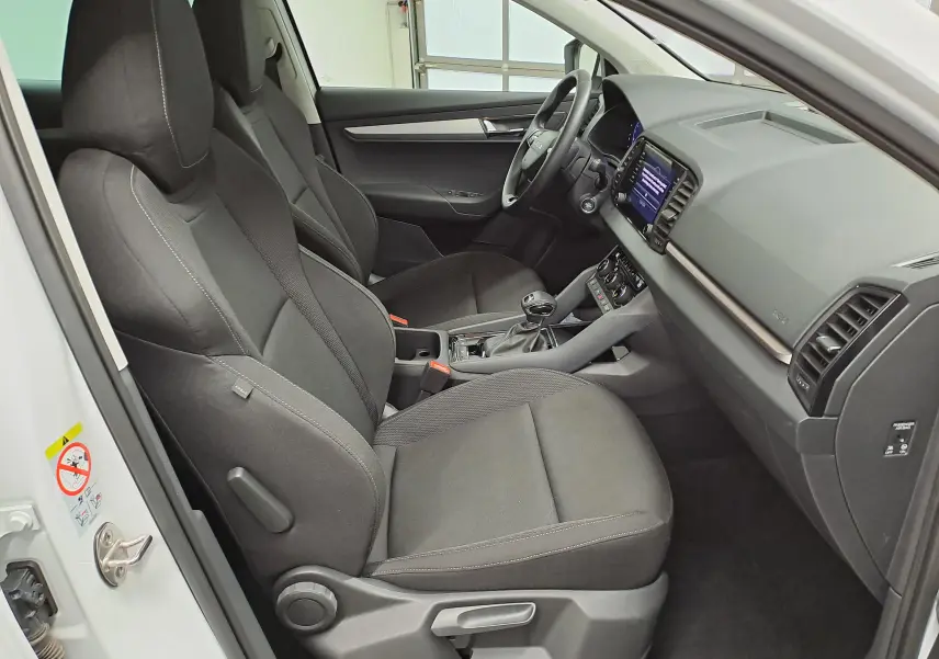 Vue intérieure côté conducteur du Skoda Karoq blanc lune 2025, montrant les sièges noirs et le tableau de bord moderne.