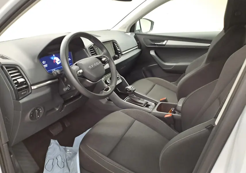 Intérieur avant droit du Skoda Karoq 2025 blanc lune, montrant le tableau de bord numérique et les sièges tissu noirs.