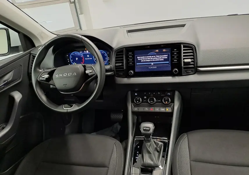 Vue intérieure avant du Skoda Karoq 2025, tableau de bord et volant noirs avec écran tactile central allumé.