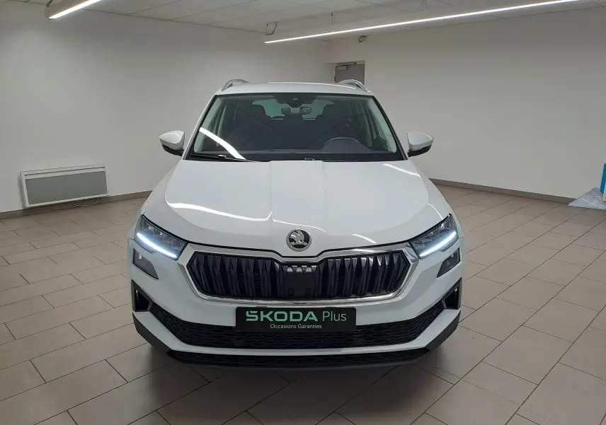 Vue frontale d'un Skoda Karoq blanc lune 2025 avec phares LED allumés et calandre noire distinctive.