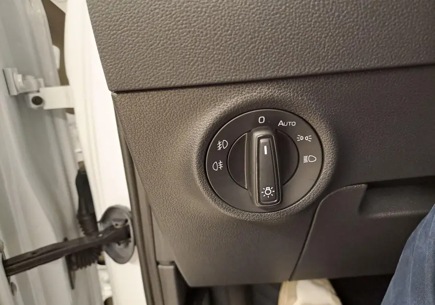 Gros plan sur le bouton de réglage des phares dans l'habitacle d'un Skoda Karoq Blanc Lune 2025, côté conducteur.