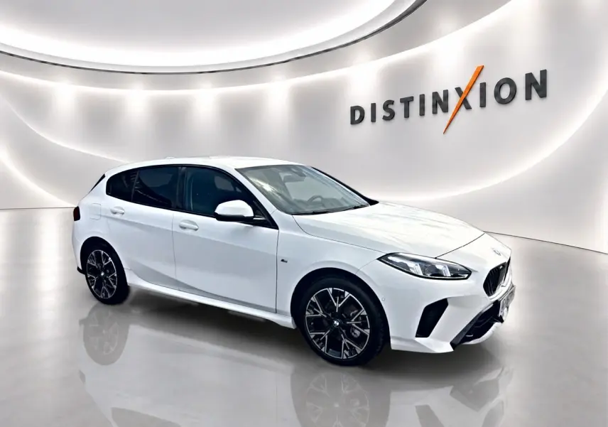 BMW Série 1 blanc pur vue 3/4 avant droit dans un showroom lumineux avec jantes noires et logo Distinxion en arrière-plan.