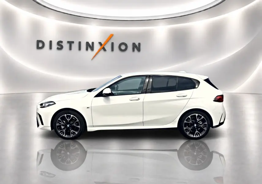 BMW Série 1 blanche vue de profil côté gauche, avec jantes noires et arrière compact en studio lumineux.