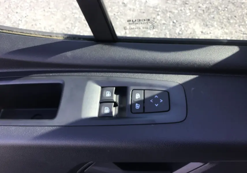 Gros plan sur les commandes de lève-vitres et réglage des rétroviseurs côté conducteur d'un Renault Master blanc.