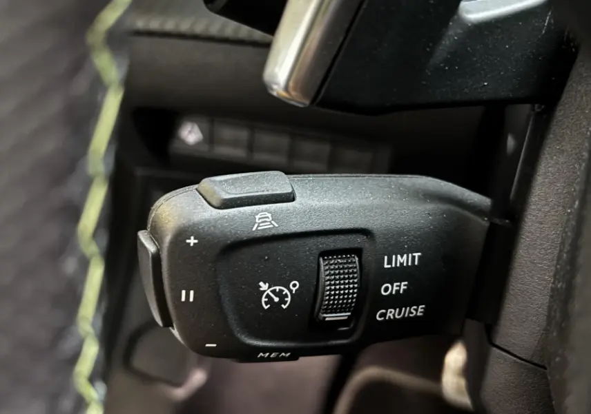 Gros plan sur la commande de régulateur de vitesse et limiteur, intérieur noir avec surpiqûres vertes du Peugeot 208 Hybrid 136 eDCS6 GT.