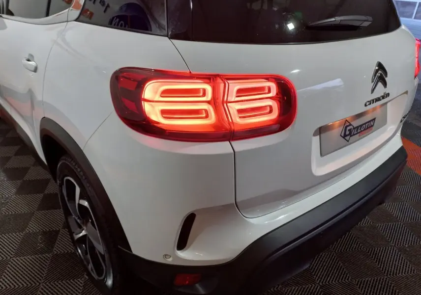 Vue 3/4 arrière droite d'un Citroën C5 Aircross blanc avec feux arrière allumés et jantes noires.