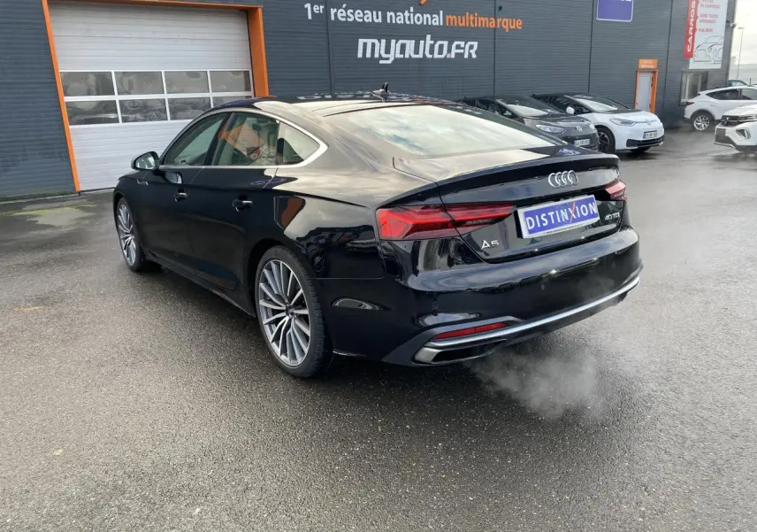 Audi A5 Sportback noir mythic métallisé vue 3/4 arrière droit, avec jantes multibranches et feux LED distinctifs.