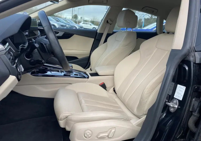 Intérieur côté conducteur d’Audi A5 Sportback 2022 noir mythic, sièges sport cuir beige et console centrale brillante noire.