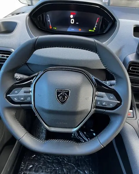 Vue rapprochée du volant cuir noir du Peugeot Rifter 2024 avec tableau de bord numérique et commandes intégrées.