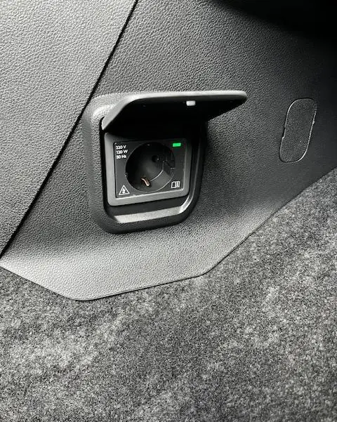 Prise électrique 220V intégrée dans le coffre gris foncé du Peugeot Rifter 2024, vue rapprochée côté droit.