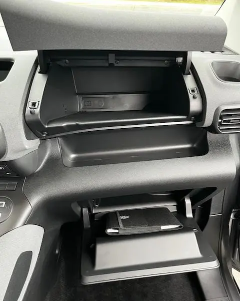 Vue intérieure du tableau de bord du Peugeot Rifter 2024 gris foncé, avec boîte à gants ouverte et rangement supérieur visible.