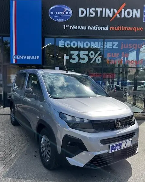 Vue 3/4 avant d'un Peugeot Rifter gris foncé stationné devant une concession avec logo Distinxion visible.