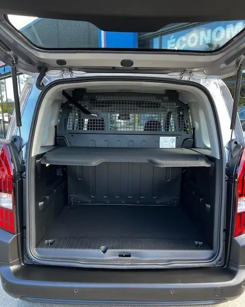 Vue arrière ouverte du Peugeot Rifter gris foncé 2024, montrant l'espace de chargement avec cloison métallique et tablette de séparation.