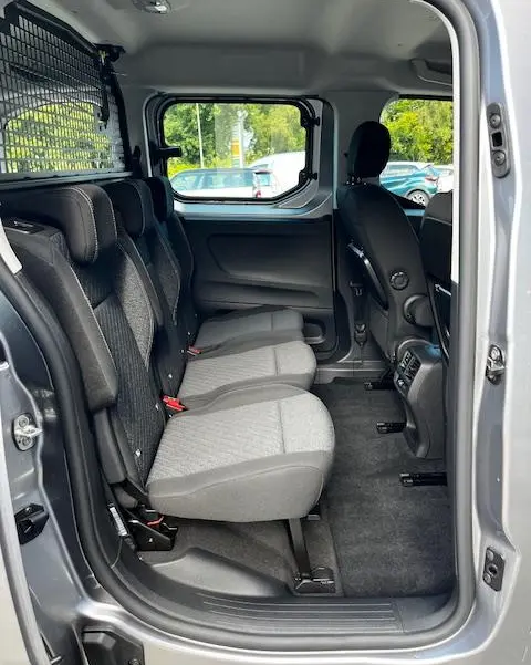 Vue intérieure côté droit du Peugeot Rifter gris foncé 2024, montrant les sièges arrière et la séparation grillagée avec le coffre.