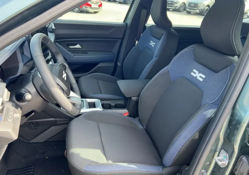 Vue intérieure côté conducteur du Dacia Bigster Hybrid 155 Expression Plus avec sièges tissu noir et bleu et accoudoir central.