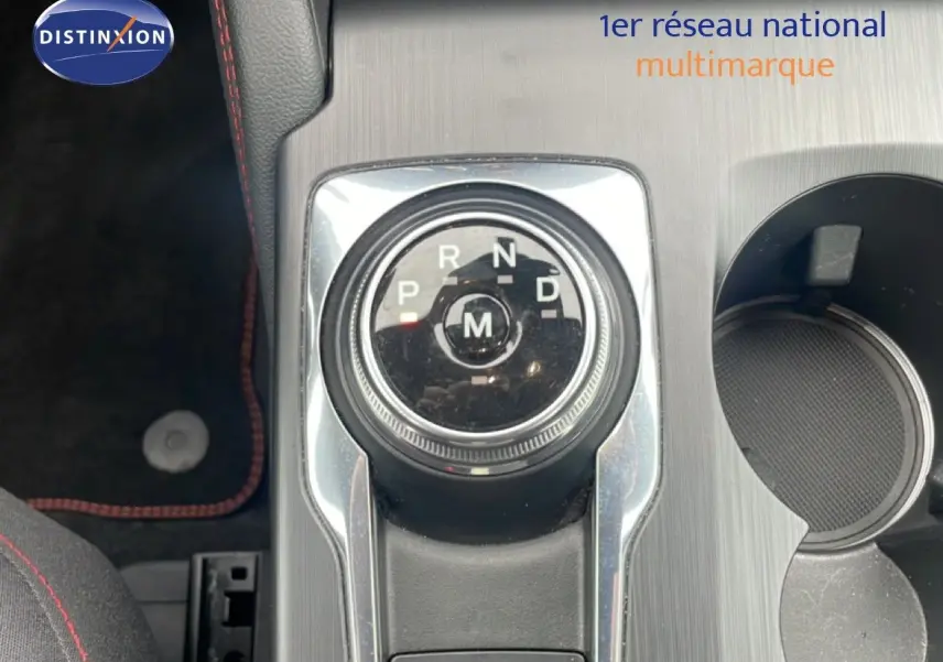 Gros plan sur la molette de boîte automatique du Ford Kuga bleu Vapor Metal, avec console grise et porte-gobelet visible.