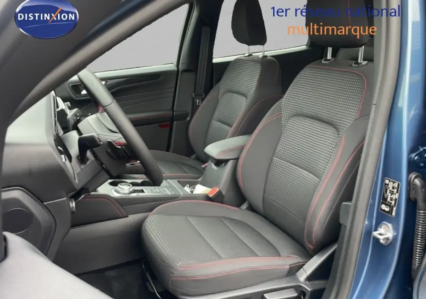 Vue intérieure côté conducteur du Ford Kuga 2024 bleu Vapor Metal, sièges tissu noir avec surpiqûres rouges et console centrale visible.