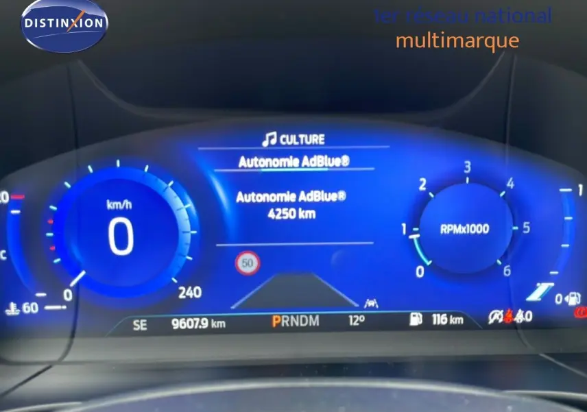 Tableau de bord numérique bleu du Ford Kuga 2024, affichant vitesse, régime et autonomie AdBlue.