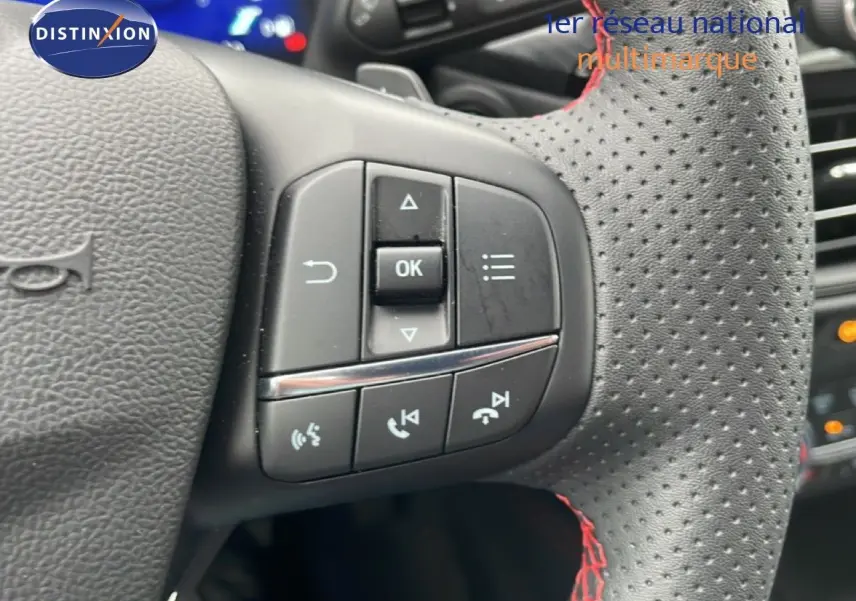Gros plan sur les commandes au volant en cuir perforé noir avec surpiqûres rouges du Ford Kuga 2024.