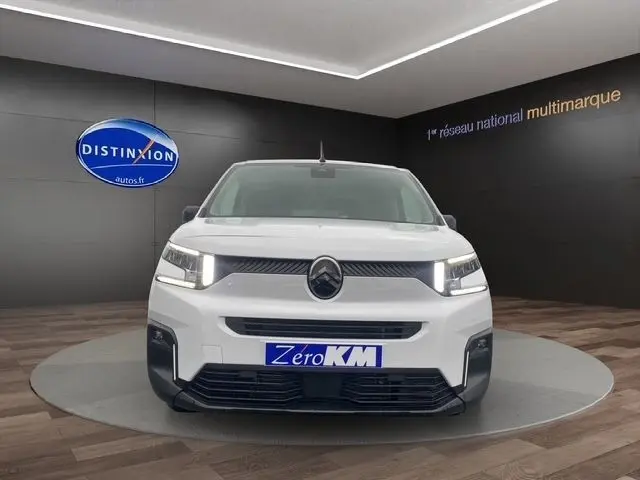 Vue frontale d'un Citroën Berlingo blanc 2025 avec phares allumés dans un showroom sombre.